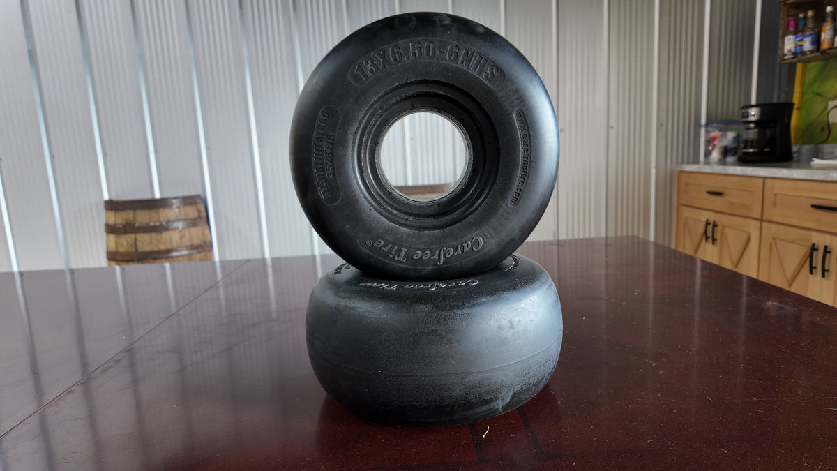 Two black rubber off-road tires stacked on top of each other on a dark wooden table, with a corrugated metal wall and kitchen cabinets in the background.