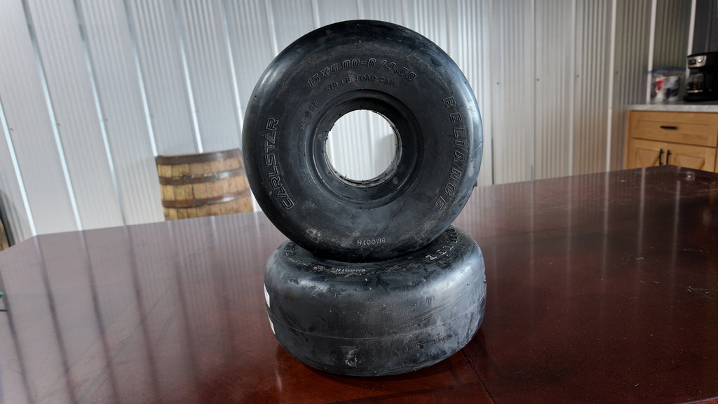 Two black rubber caster wheels stacked on a dark wooden table, with a corrugated metal wall and a wooden cabinet in the background.